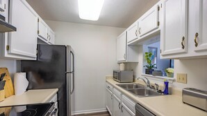 A compact kitchen with white cabinets, stainless steel appliances, and a window with a view. - Keystone Garden Villa B (Indianapolis)