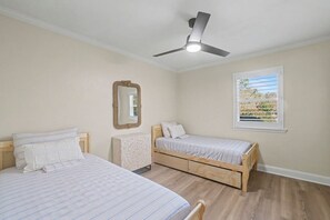 Ein Schlafzimmer mit zwei Betten, einem Deckenventilator, einem Fenster mit Jalousien und einem Spiegel an der Wand.