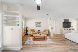 Ein Wohnzimmer mit Couchtisch aus Holz, zwei Sesseln, einem Fernseher und einem Bücherregal.