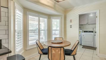 A kitchen with a dining area, featuring a round table with chairs, a built-in oven, and a window with blinds.