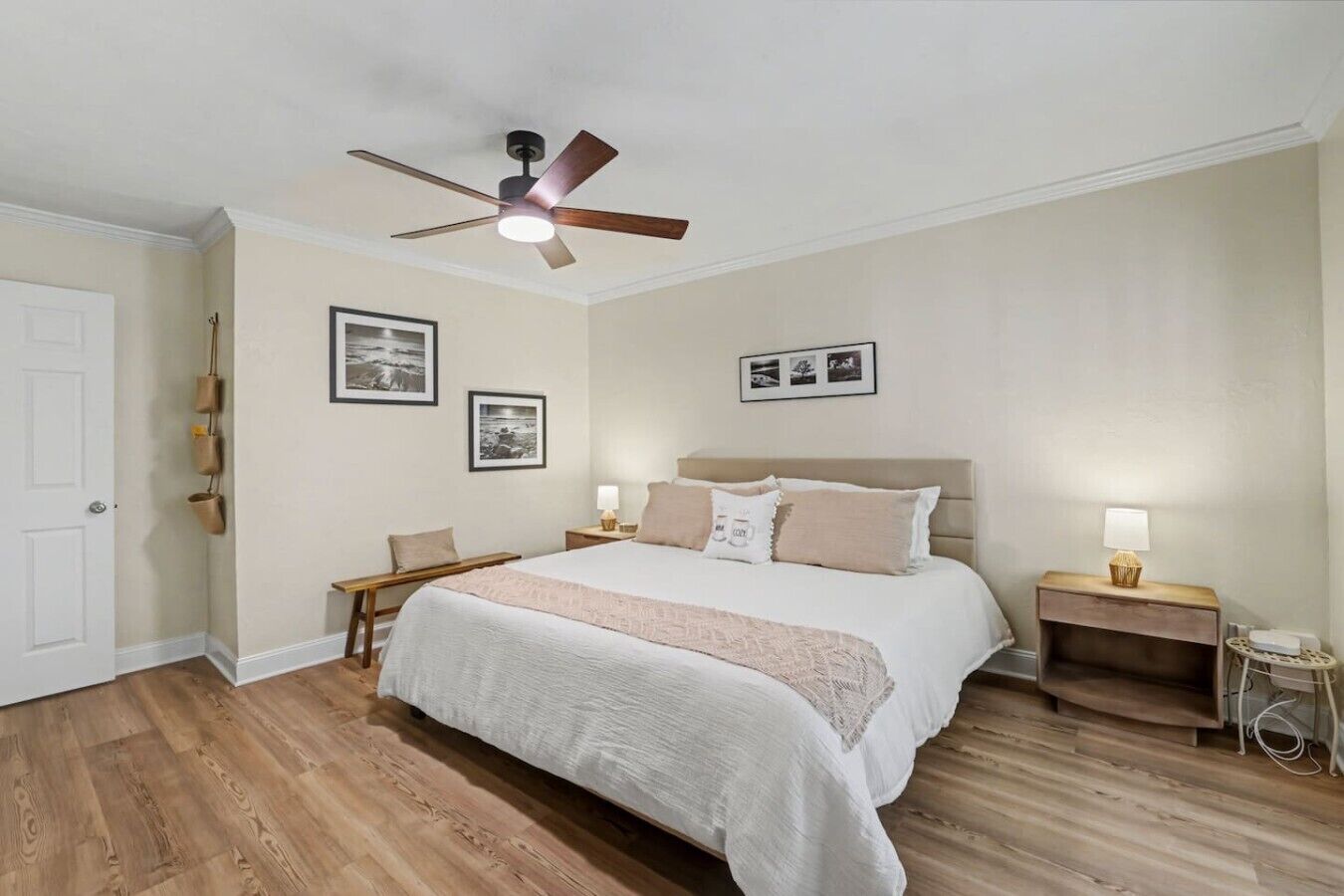 A bedroom with a bed, a ceiling fan, a nightstand with a lamp, and a door.