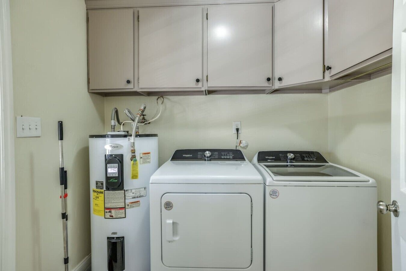 A laundry room with two Whirlpool washers and a water heater.