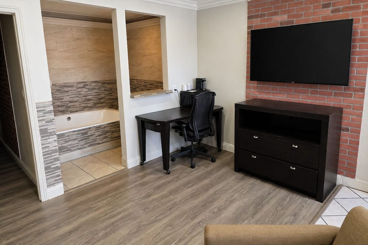 A modern room with a desk, chair, TV, and a brick wall.