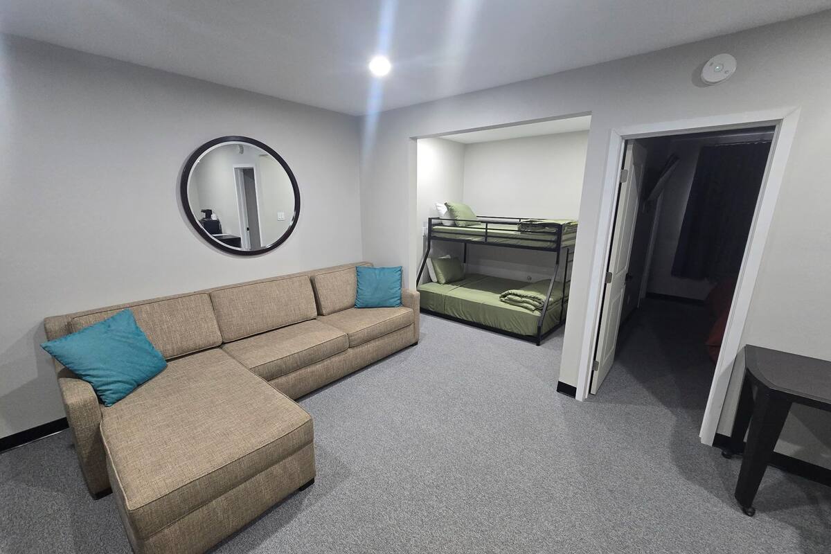 A living room with a sofa, a bunk bed, a round mirror, and a door leading to another room.