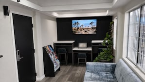 Uma sala de estar moderna com um sofá cinza, uma TV fixada na parede, uma escrivaninha com um laptop e uma planta.