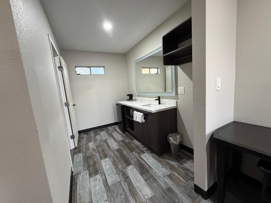 Un baño con piso de madera, lavamanos blanco, espejo y perchero.