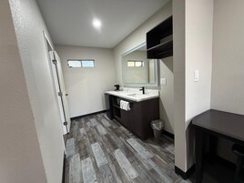 Un baño con piso de madera, lavamanos blanco, espejo y perchero.
