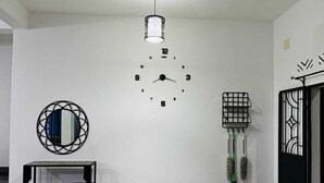 Una stanza con una sveglia a muro, uno specchio, un tavolino con sedie e una porta con un cancello decorativo.