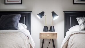 Een hotelkamer met twee bedden, een nachtkastje met lampen, en lijstjes met foto's aan de muur.