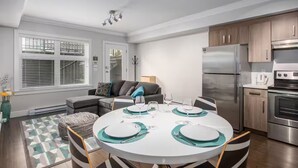 Een moderne keuken met roestvrijstalen apparatuur, een eethoek met een ronde tafel, en een grijze bank.