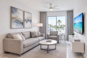 A modern living room with a sofa, armchair, coffee table, and a TV on a stand. - Coastal Breeze Suite on Bayfront (Clearwater)