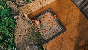 Een houten terras met een patroonmat, omringd door begroeiing en rotsachtig terrein.
