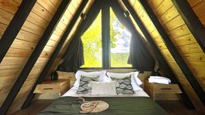Een kamer met hoge plafonds en een schuin houten dak, een groot bed met wit beddengoed en een raam met gordijnen.