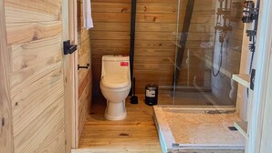 Een kleine badkamer met houten lambrisering, een toilet, een douche en een zichtbare toiletborstel.