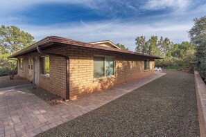 A single-story house with a brick exterior, a gravel driveway, and a small patio area. - Flaming Arrow: Zen Retreat, Close to Hiking/Shops (Sedona)