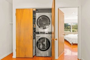 A laundry room with two washing machines, a wooden door, and a view of a bedroom with a bed. - Flaming Arrow: Zen Retreat, Close to Hiking/Shops (Sedona)