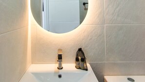 Une salle de bain avec un lavabo blanc, un miroir rond et des toilettes.