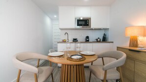 Une cuisine moderne avec des meubles blancs, un four à micro-ondes et une machine à café. On y trouve une table à manger avec des chaises et une lampe sur le côté.