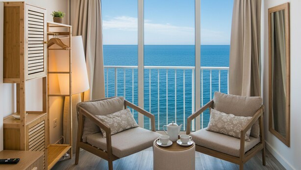 Un balcon avec deux chaises, une petite table avec des tasses et une théière, une lampe, et une vue sur la mer.