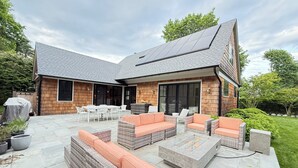 Una casa moderna con un patio attrezzato con mobili da esterno, un caminetto e una zona barbecue coperta.