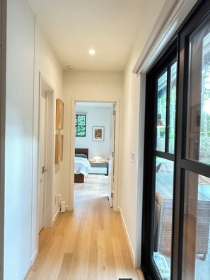 A hallway leading to a bedroom with a bed, bedside table, and a window. - US Open Golf Championship Rental - modern 4-bedroom house in serene East Hampton (East Hampton)