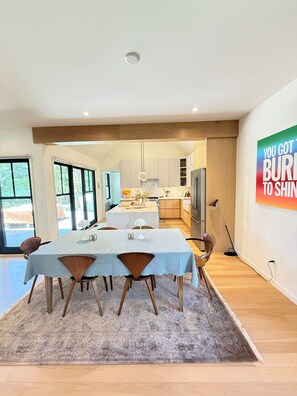 A modern kitchen with a central island, wooden cabinets, and a dining area with a table and chairs. - US Open Golf Championship Rental - modern 4-bedroom house in serene East Hampton (East Hampton)