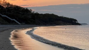 Una spiaggia con un litorale curvilineo, una scala che conduce a una zona boschiva e un mare calmo.