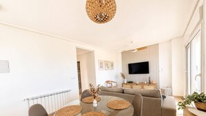 A modern living room with a glass dining table, grey sofas, and a flat-screen TV mounted on the wall. - Apartment for 4 people - golf course view - La Torre Golf Resort (Torre-Pacheco)