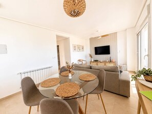 Ein modernes Wohnzimmer mit einem Glastisch, grauen Sofas und einem flachbildfernseher an der Wand.