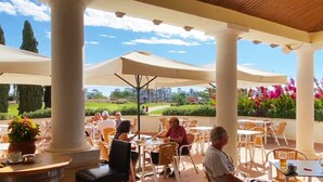 An outdoor café with tables and chairs, large umbrellas, and a view of a golf course. - Apartment for 4 people - golf course view - La Torre Golf Resort (Torre-Pacheco)