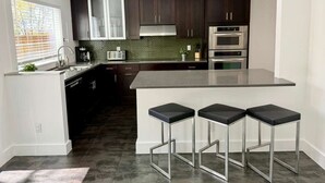 A modern kitchen with dark cabinets, stainless steel appliances, and a central island with bar stools. - King William Historic District Cozy 3BR SATX (San Antonio)