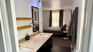 A hotel room with a bathroom, a bed, a small table, and a window with curtains. - King William Historic District Cozy 3BR SATX (San Antonio)