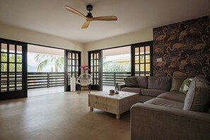 Ein geräumiges Wohnzimmer mit einer Couch, einem Couchtisch, einem Deckenventilator und Blick durch große Fenster.