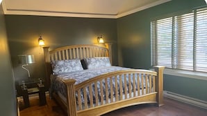 Quarto com cama de madeira curva, duas luminárias de cabeceira, mesa de cabeceira e janela com persianas.