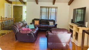 Uma sala de estar com sofá em formato de L, televisão e aparador de madeira.