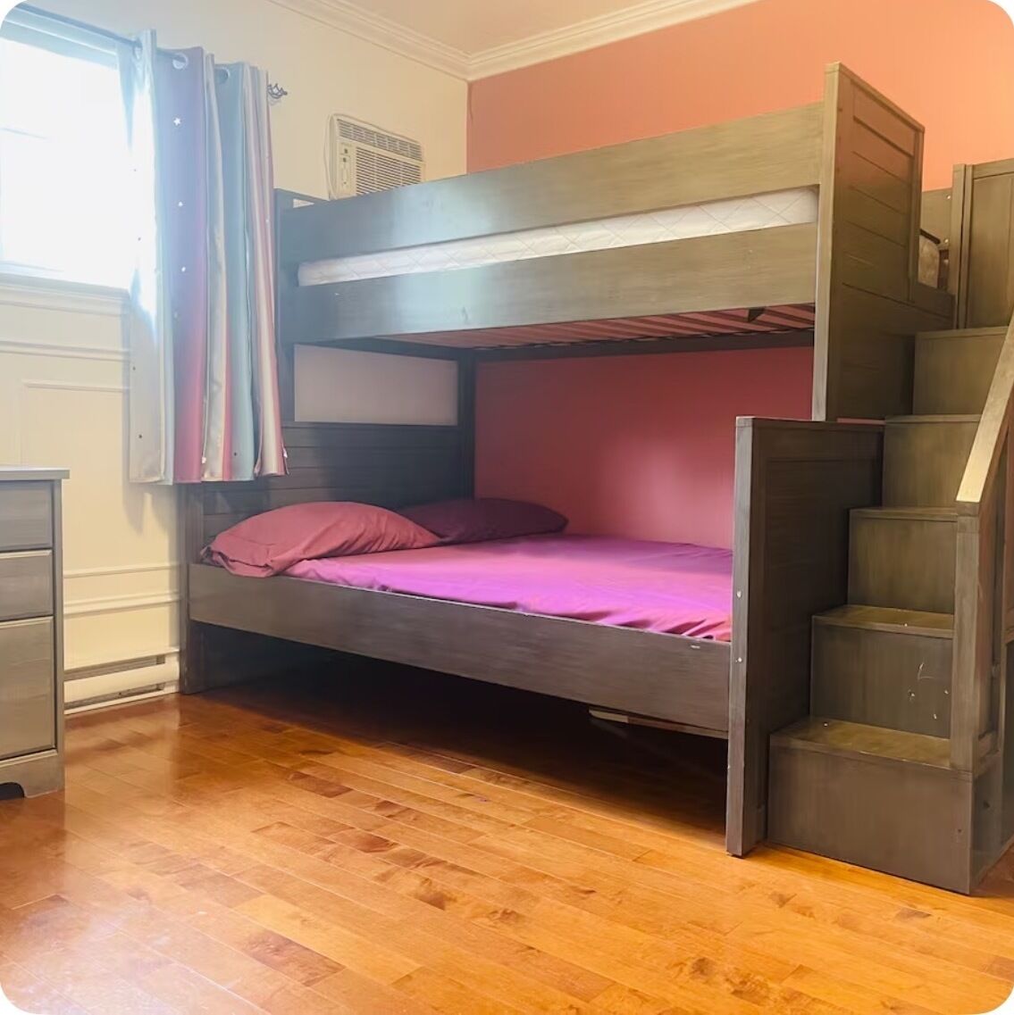A bunk bed with a wooden frame, a pink mattress, and a staircase on the right.