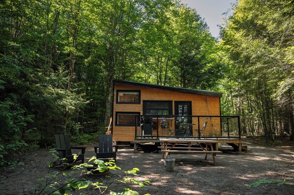 Une cabane dans une forêt, avec une terrasse, des chaises et une table.