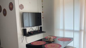 A dining area with a black table, matching benches, and a TV mounted on the wall.