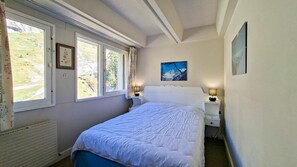 Ein Schlafzimmer mit einem Bett, zwei Nachttischen, einem Fenster mit Vorhängen, einer Heizung und einem Gemälde an der Wand.