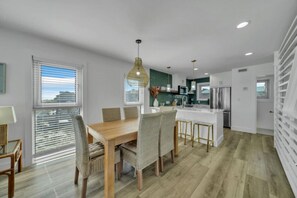 Une cuisine moderne dotée d’un îlot central, d’un coin repas avec des chaises en osier et offrant une vue sur la ville grâce à de grandes fenêtres.