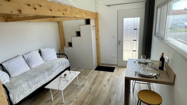 A compact room with a bed, a small table, a chair, a staircase, and a window. - Detached 2-star studio, sleeps 4, very quiet, close to the seafront (Pisany)