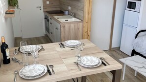 A modern kitchen with a dining area set for four, featuring wooden cabinets, a built-in oven, and a microwave. - Detached 2-star studio, sleeps 4, very quiet, close to the seafront (Pisany)