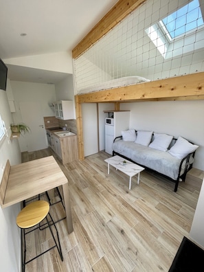 A compact living space with a kitchenette, a sofa, a dining table, and a small stool.