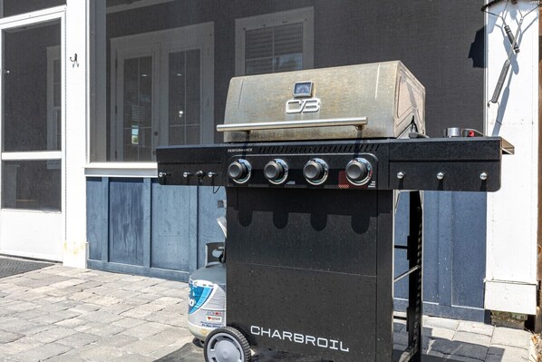Un barbecue au charbon de bois doté de quatre brûleurs et d’un écran numérique, portant l’inscription « CHARBROIL », placé à l’extérieur d’un bâtiment avec une porte et des fenêtres bleues.