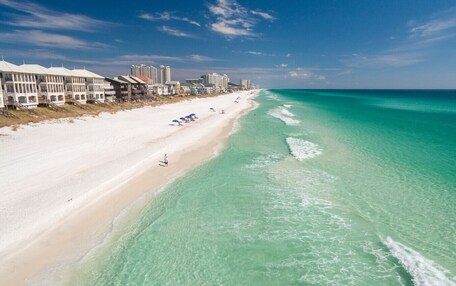 A beach with a row of white buildings, clear turquoise water, and a sandy shore.