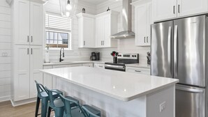 Cozinha moderna com armários brancos, geladeira de aço inoxidável, ilha central com banquetas e iluminação pendente.