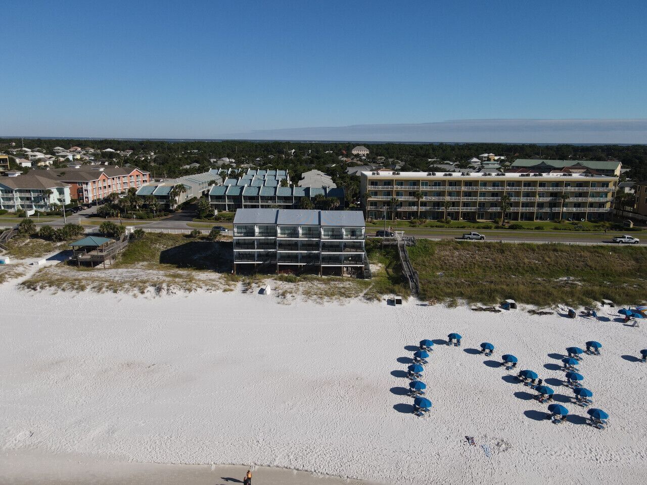 Un hôtel situé en bord de mer, composé de plusieurs bâtiments, avec une plage de sable et des parasols disposés en rangées.
