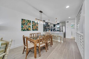 Une cuisine moderne dotée d’un îlot central, de luminaires suspendus et d’un coin repas avec une table à plateau en verre et des chaises en osier.
