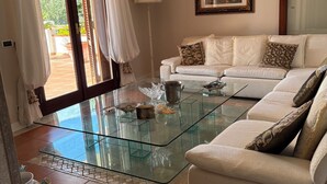 Un salon avec une table basse en verre, un canapé blanc et un tableau accroché au mur.