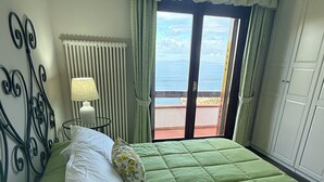 Une chambre avec un lit, une lampe, un radiateur, une fenêtre avec des rideaux et une vue sur la mer.